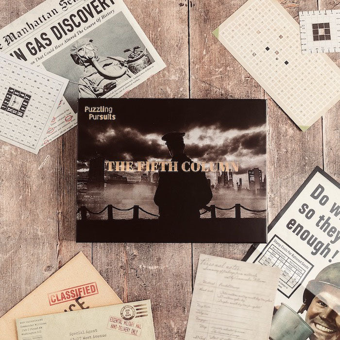 The Fifth Column game box on a wood table surrounded by a Manhattan newspaper page about a gas discovery, punched decoder cards, a wartime poster, handwritten personal notes and a kraft envelope stamped CLASSIFIED