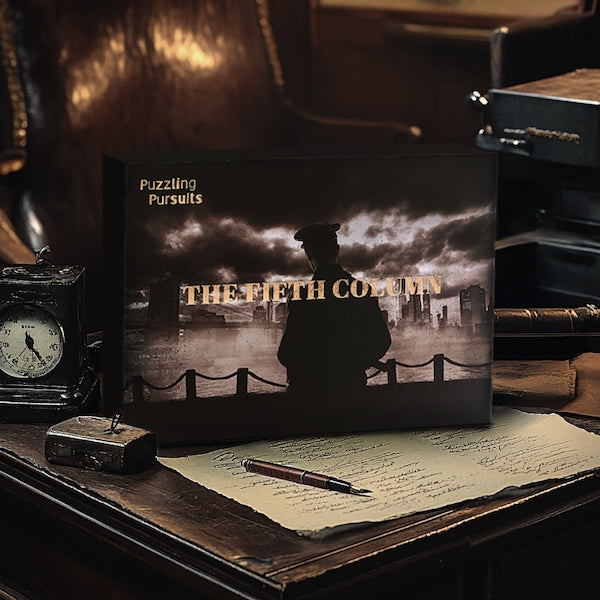 The Fifth Column box standing on a dark wooden desk beside a small vintage travel clock and a page of handwriting with a fountain pen resting on it. The box cover shows a figure in a peaked cap silhouetted against a smoky city skyline.