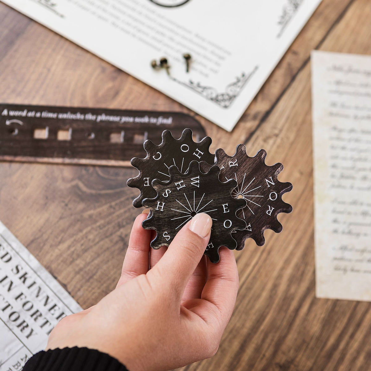 A brass cog cipher wheel from Origins & Ends held in one hand, an example of a substitution-cipher escape room puzzle