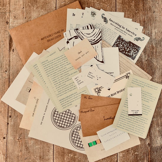Murder mystery game materials scattered across a wooden table: a kraft envelope labelled 'Materials found on Bruno Costa', newspaper clippings, typed documents and handwritten notes