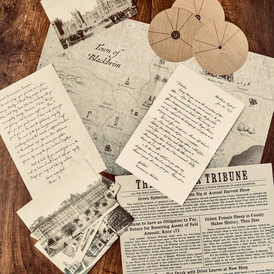 Blackbrim: 1876 Part I materials spread on a wooden table: a town map, handwritten letters, newspaper pages, photograph cards and two wooden cipher discs